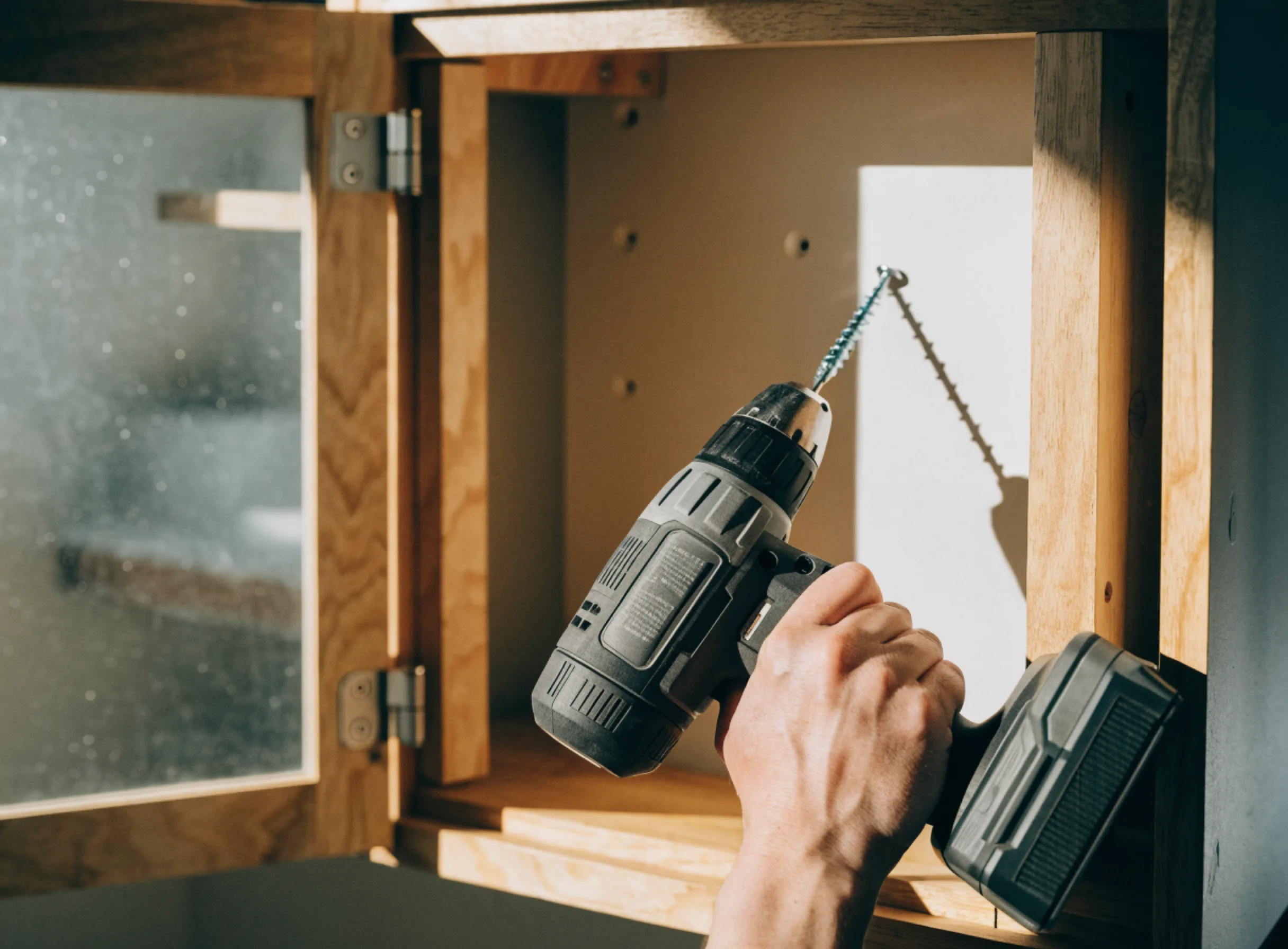 A wall cabinet being screwed through its hanging rail into the framing behind the drywall