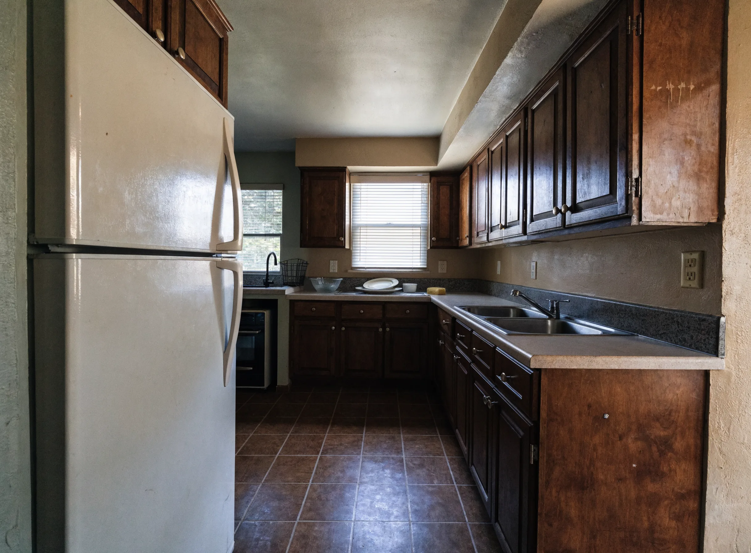 An older Florida kitchen still in daily use, with a narrow walkway, a boxed soffit above the upper cabinets and laminate counters