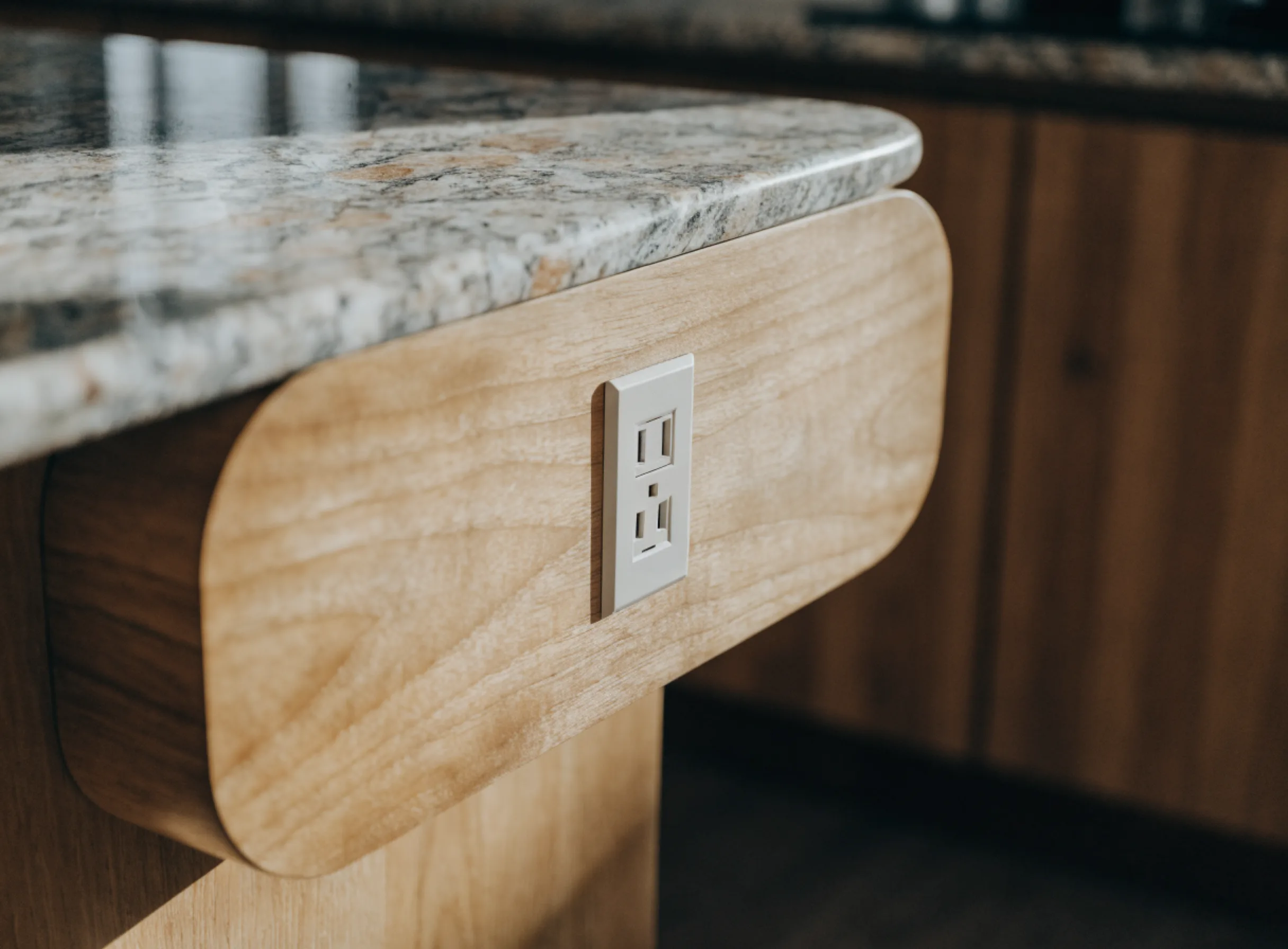 A receptacle set into the end panel of a kitchen island, with the cable run reaching it from below