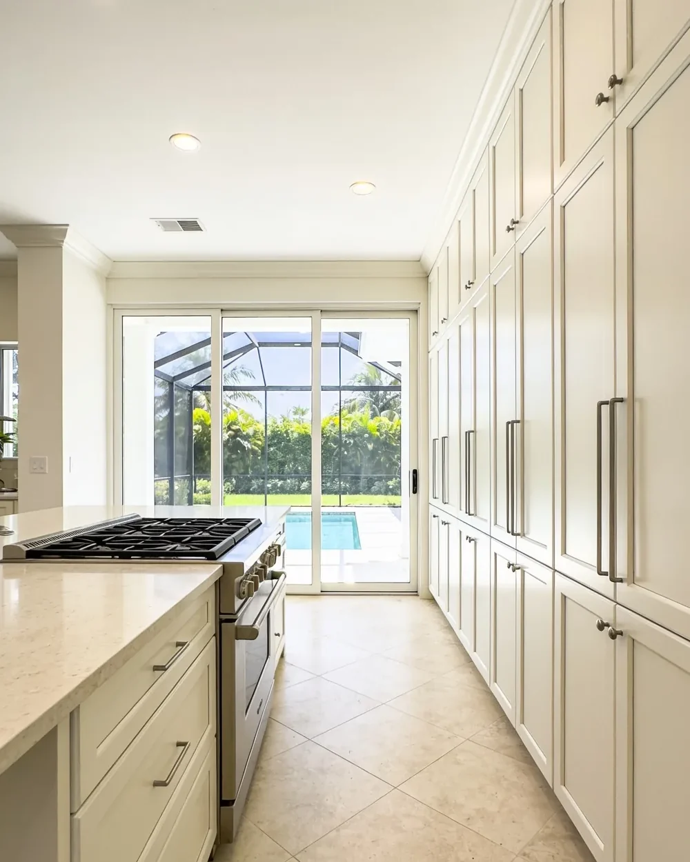 Kitchen remodeler near Boca West Country Club: a villa kitchen with pale cabinetry and wide sliding glass doors onto a screened terrace