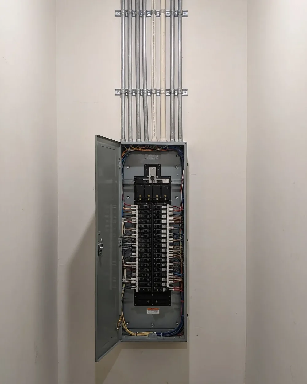 A newly installed electrical panel with the door open, neatly arranged breakers and new conduit run up the wall