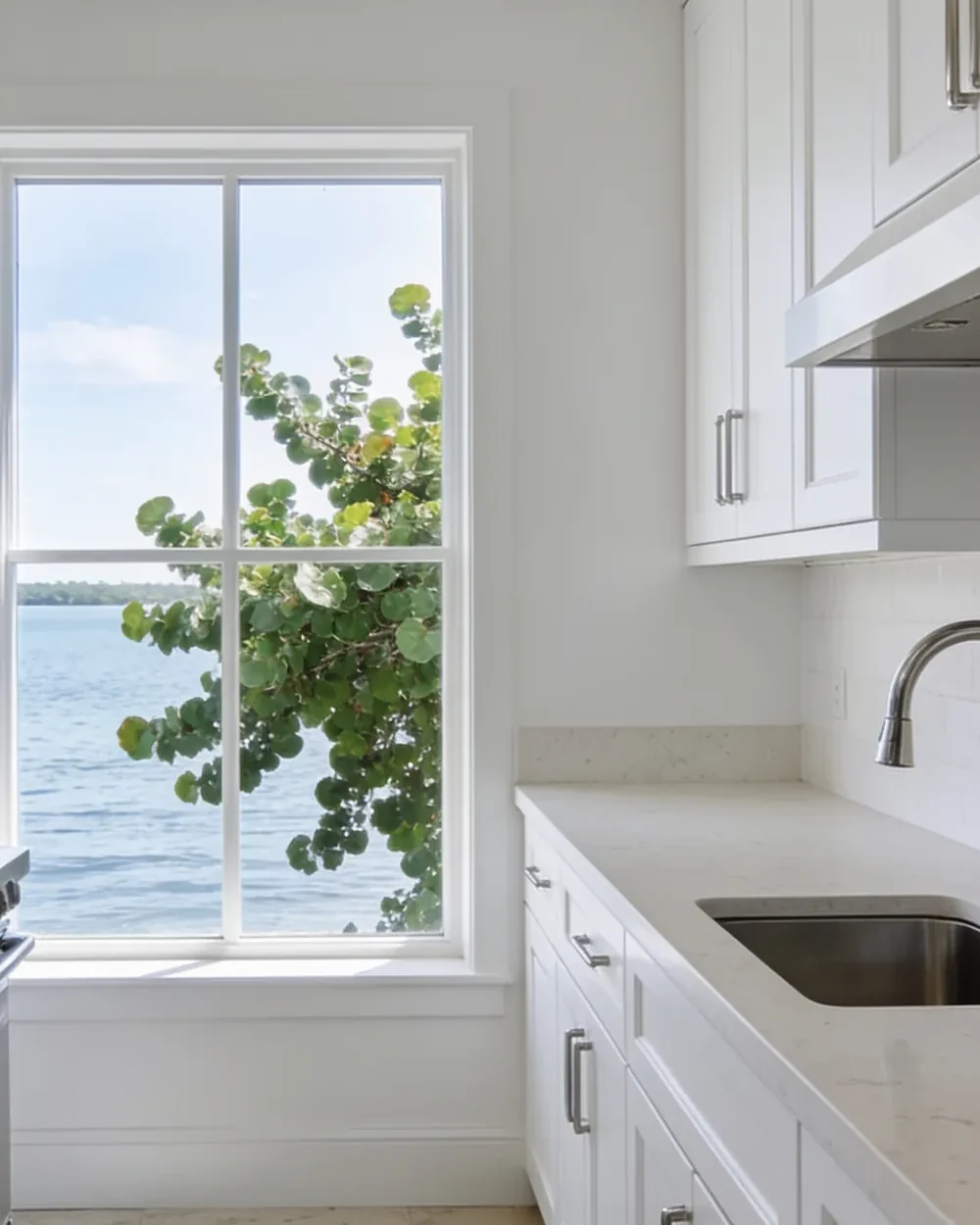 Kitchen remodeler near Gumbo Limbo Nature Center: a coastal kitchen with white cabinetry, a pale quartz counter and a wide window looking onto water and sea grape