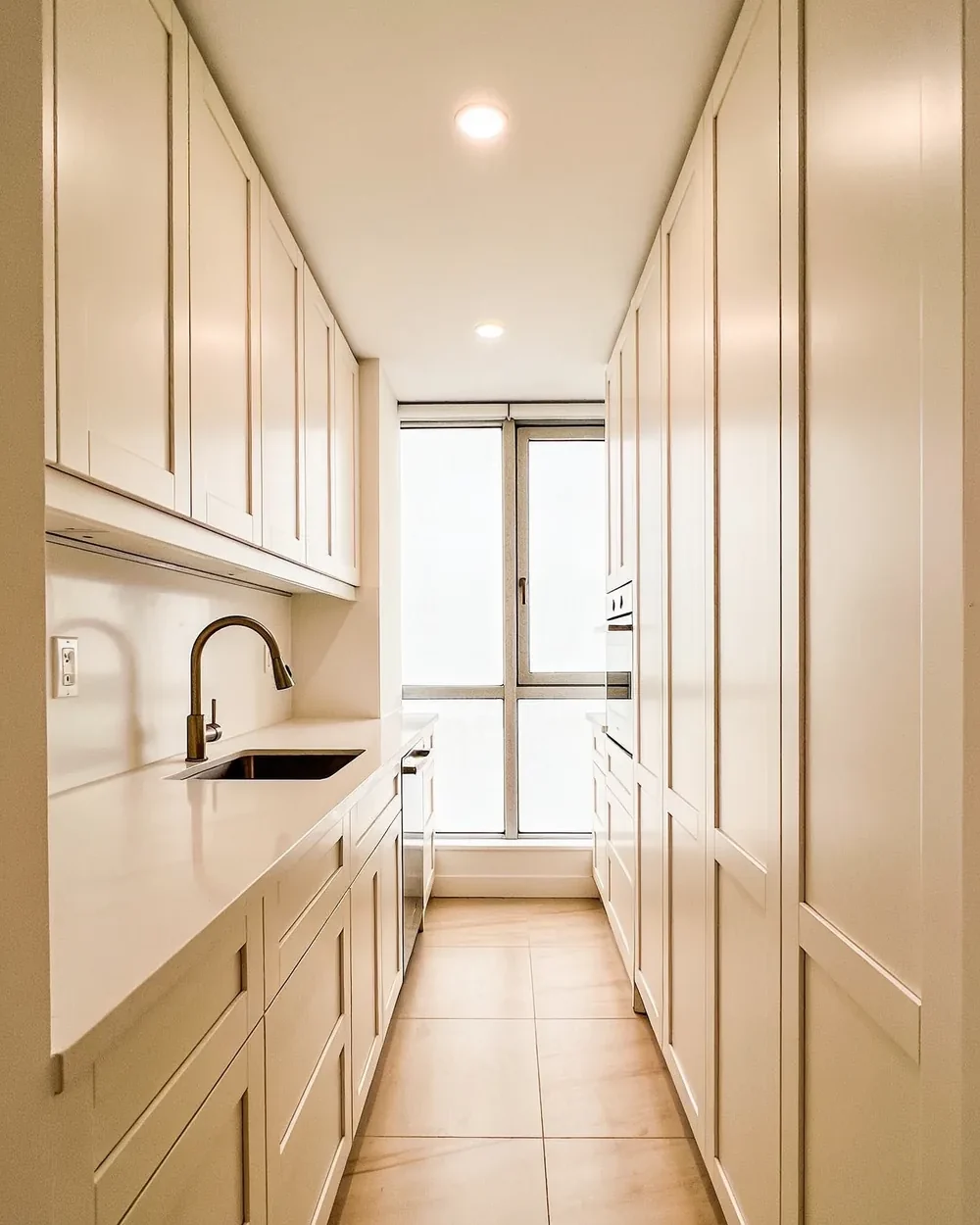 Kitchen remodeler near Mizner Park: a compact galley kitchen in a mid rise apartment, with pale cabinets carried to the ceiling and a window at the end of the run