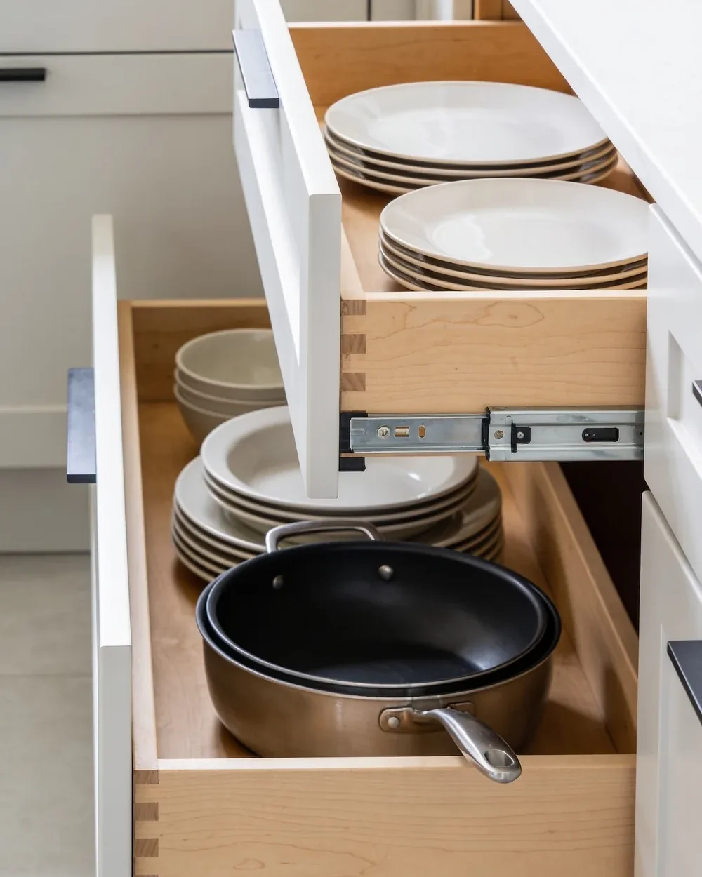 Deep kitchen drawers pulled fully open, showing stacked dishes and pans on birch drawer boxes