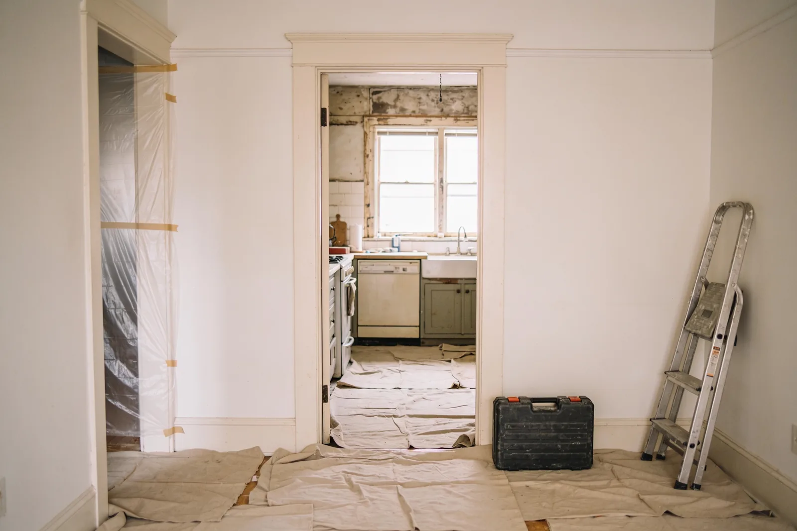 A kitchen doorway on the first morning of a remodel, with drop cloths down and a tool case against the wall