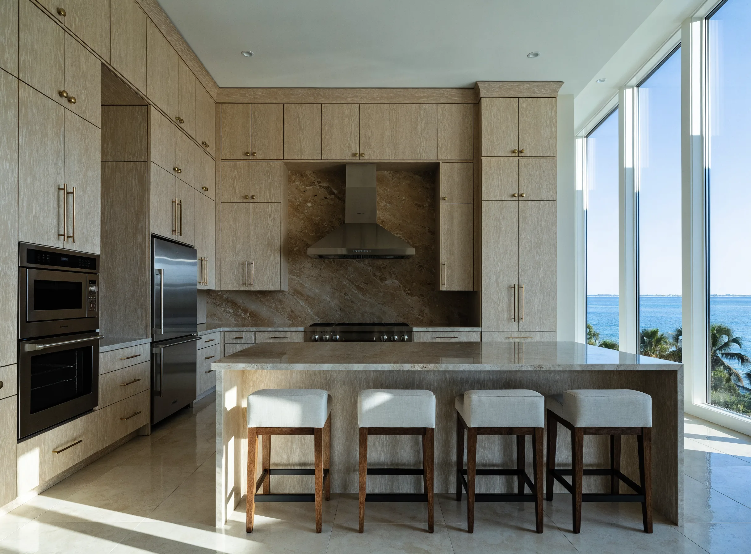 Luxury kitchen remodeling Boca Raton: a finished kitchen with full-height pale oak cabinetry, a long island and a stone slab backsplash behind the range